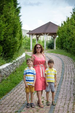 Genç bir kadın çocuklarıyla parkta oynarken eğleniyor. İlkokul çağındaki çocuklar. Aile pitoresk bitkilerle çevrili. Açık hava oyunları herkes için kullanışlı.