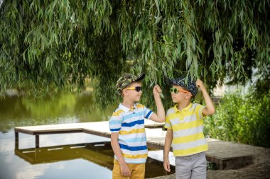 Kardeşlerim, kardeşlerim, sarılın. İki çocuk, büyük oğlan ve küçük kardeşi gölün kıyısında yaşlı ağacın yanında duruyorlardı. Yaz tatili kavramı. Doğada boş zaman..