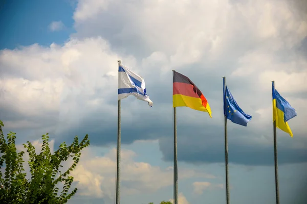 The flag of the European Union and flags of Ukraine, Israel, Germany flutter in the wind in different directions against the blue sky. Bottom side view.