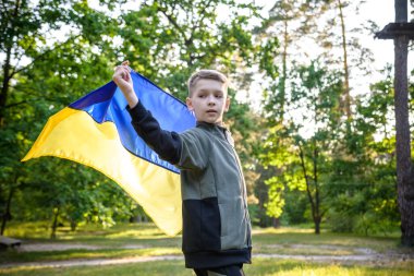 Ukrayna için dua et. Yaz parkını yöneten Ukrayna bayrağı taşıyan bir çocuk. Ulusal bayrak sallayan küçük çocuk barış için dua ediyor. Bağımsızlık Günü 'nü kutlayan mutlu çocuk.