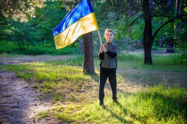 Ukraynalı çocuk elinde bayrak sallayarak Ukrayna 'daki savaşı gün batımında durdurmak için dua ediyor. Rusya 'nın Ukrayna' ya karşı savaşı. Savaşı Durdur.