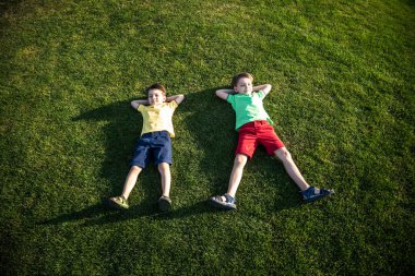 Parkta eğlenen iki kardeşin fotoğrafı, yeşil çimenlere uzanan iki neşeli çocuk, dışarıda oynayan küçük çocuk, en iyi arkadaşlar, mutlu aile, aşk ve mutluluk konsepti..