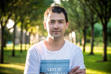 Açık havada beyaz gömlekli, doğa parkında gülümseyen güzel bir adamın portresini kapat. Moda modeli.