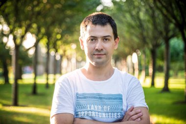 Açık havada beyaz gömlekli, doğa parkında gülümseyen güzel bir adamın portresini kapat. Moda modeli.