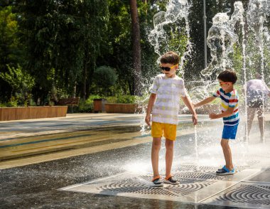 Çocuk çeşmelerde eğleniyor. Sıcak bir yaz gününde şehir çeşmesiyle oynayan bir çocuk. Fıskiyede eğlenen mutlu çocuklar. Yaz havası. Aktif eğlence, yaşam tarzı ve tatil.