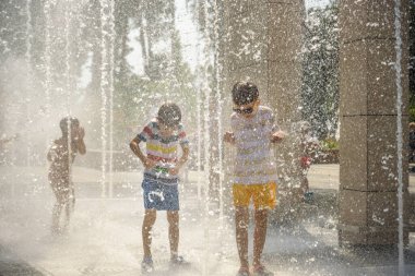 Çocuk çeşmelerde eğleniyor. Sıcak bir yaz gününde şehir çeşmesiyle oynayan bir çocuk. Fıskiyede eğlenen mutlu çocuklar. Yaz havası. Aktif eğlence, yaşam tarzı ve tatil.