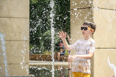 Çocuk çeşmelerde eğleniyor. Sıcak bir yaz gününde şehir çeşmesiyle oynayan bir çocuk. Fıskiyede eğlenen mutlu çocuklar. Yaz havası. Aktif eğlence, yaşam tarzı ve tatil.