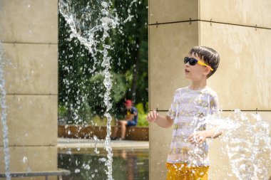 Çocuk çeşmelerde eğleniyor. Sıcak bir yaz gününde şehir çeşmesiyle oynayan bir çocuk. Fıskiyede eğlenen mutlu çocuklar. Yaz havası. Aktif eğlence, yaşam tarzı ve tatil.