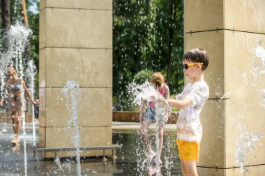 Çocuk çeşmelerde eğleniyor. Sıcak bir yaz gününde şehir çeşmesiyle oynayan bir çocuk. Fıskiyede eğlenen mutlu çocuklar. Yaz havası. Aktif eğlence, yaşam tarzı ve tatil.