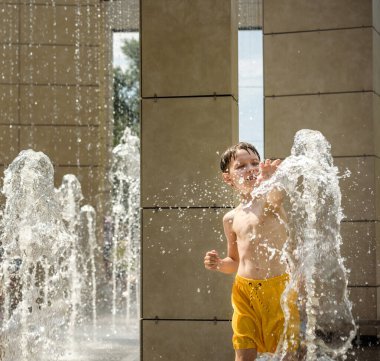 Çocuk çeşmelerde eğleniyor. Sıcak bir yaz gününde şehir çeşmesiyle oynayan bir çocuk. Fıskiyede eğlenen mutlu çocuklar. Yaz havası. Aktif eğlence, yaşam tarzı ve tatil.