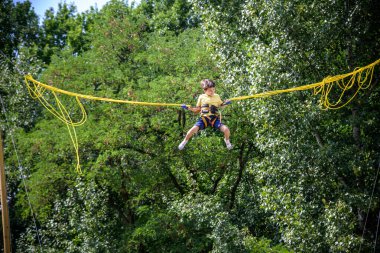 Çocuk bungee trambolinde zıplıyor. Sigortası ve esneyebilir lastikleri olan bir çocuk gökyüzüne asılı duruyor. Eğlence parkında mutlu çocukluk ve oyun kavramı.
