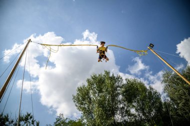 Çocuk bungee trambolinde zıplıyor. Sigortası ve esneyebilir lastikleri olan bir çocuk gökyüzüne asılı duruyor. Eğlence parkında mutlu çocukluk ve oyun kavramı.