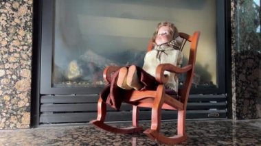 Eski ve çok garip bir bebek şöminenin arka planında sallanan bir sandalyede oturuyor, çok korkunç bir şekilde sallanıyor, sanki bir korku filminde, sanki 07.2022 Kanada Vancouver 'da bir şey olmuş gibi. 