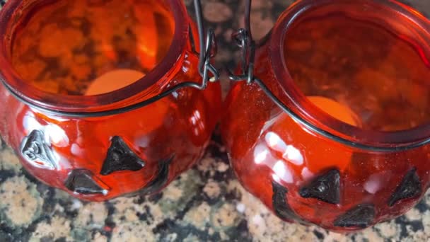 两个明亮的橙色烛台 形状是南瓜杰克O灯玻璃灯笼真正的蜡烛黑色的眼睛和黑色的微笑透明的橙色玻璃杯站在壁炉前 — 图库视频影像