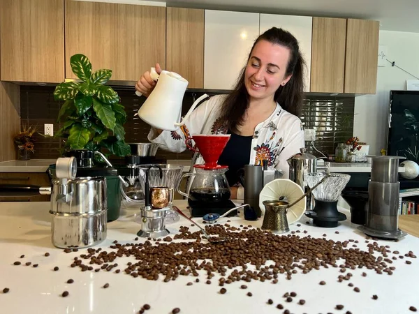 Beautiful young woman with black hair pours water Different professional coffee equipment on the table next to the coffee flower as well as different accessories for brewing coffee Craft ad