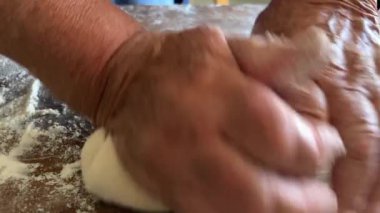 Yaşlı bir kadının yaşlı elleri hamuru yuvarlar ve bir şeyler pişirir ya da hamur köftelerini ya da hamur köftelerini ahşap bir yüzeyde kaynatır. Yüksek kalite 4k görüntü
