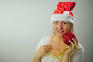 Yeni yılınız kutlu olsun. Yeni yıl partisi davetiyesi. Beyaz arka planda oturan yetişkin bir kadın Noel ağacı oyuncaklarına gülümsüyor.