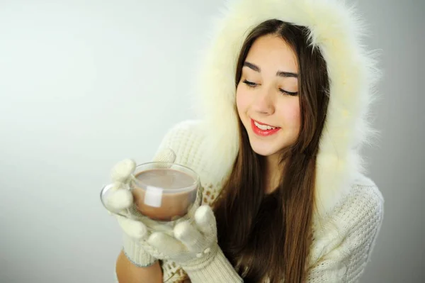 To advertise New Year warming drinks tea and coffee Beautiful young girl drinks from a glass cup of coffee or cocoa White coat and white gloves Snow Maiden with long hair put on a hood Place for text