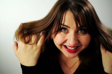 Genç bir kadın yüzünde gülüyor, gülümsemesi ve gözleri parıldıyor. Yetişkin kıvrımlı, güzel bir kadın çerçeveye bakıyor. Siyah elbisesi ve kırmızı ruju var.