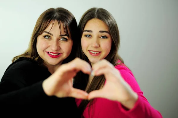 Mom and daughter show heart from hands They look into the frame touching their fingers family warmth Love and friendship Girls 17 18 years old woman 35-40