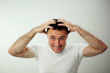 Kırışık alın, dil, farklı neşeli pozitif duygular yetişkin adamın siyah saçı komik mavi gözler beyaz tişört gri arka plan kıllı erkek elleri eğlenceli tatil seyahati kazanır