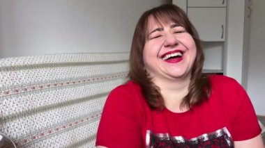 Güzel, olgun, kıvrımlı bir kadının dans edişinin olumlu yönleri parmaklarıyla güldüğü ve çok mutlu olduğu bir şeyi gösteriyor. Beyaz bir ceket ve kırmızı bir tişört giyiyor.