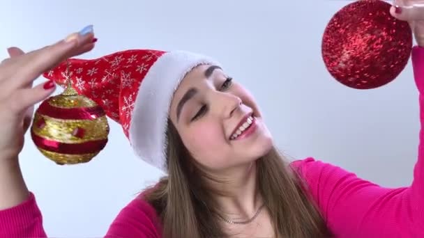 女孩手里拿着新年玩具 面带微笑地看着镜头 背景是白色的 戴着一顶帽子 粉色的夹克 手里拿着新年玩具 — 图库视频影像