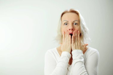 Olumlu ve olumsuz duygular. Kadın, beyaz tişörtlü sarı saçlı ve elleri açık şekilde ağzını kapatmasına şaşırdı. Sürpriz galibiyet sürprizi.