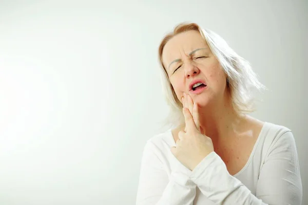 stock image An adult woman has a toothache, she presses her hand to her cheek Toothache blonde woman in all white stands against the background in clinic dentist Health disorders waiting for the doctor