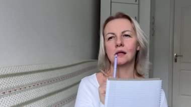 Olumlu duygular elinde kalem ve not defteri olan yetişkin bir kadın bir şeyler yazar ve düşünür. Yaratıcılık, güzel bir kadının yüzüne sarı saç ve gülümseme koyar.