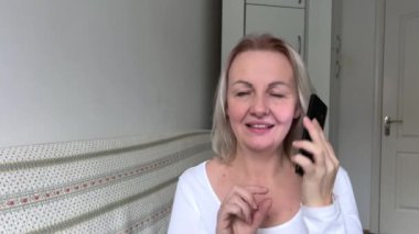 Evde cep telefonuyla konuşan bir kadın. Ofis masasında konuşan orta yaşlı beyaz bir kadın.