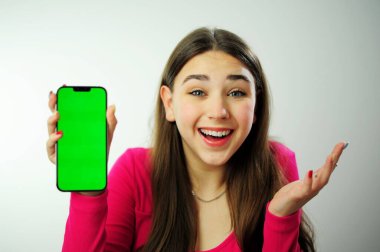 Pembe kazaklı bir kadın, çok renkli manikürlü, uzun saçlı. Telefonunu mavi gözleriyle göstermekten mutlu. Reklamcılıktan mutlu.