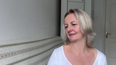 Beyaz saçlı yetişkin bir kadın, gülümseyen birine not defteri ya da not defteri verir. 35-45 yaşlarındadır.