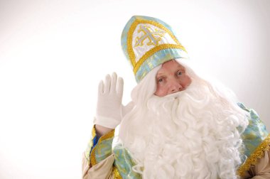 Aziz Nicholas 'ın el sallaması Sinterklaas portresi beyaz arka planda Hollandalı Noel Baba Aziz Nicholas' ın yeni yıl altınları mavi başlıklı gür sakallı ve beyaz bıyıklı beyaz eldivenli.