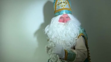 Turkuaz bir elbisesi, uzun beyaz sakalı ve Sinterklaas portresi olan bir şapkası var. Noel Baba Aziz Nicholas 'ın Noel Baba' sı. Yavaşça yürür ve çerçevenin içine bakar. Parmağını bize gösterir.