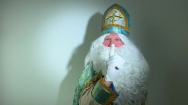 Dikkat, turkuvaz, altın rengi takım elbise, uzun beyaz sakal ve haçlı aziz şapkası olan bir kalbi gösteriyor. Sinterklaas 'ın yeni yıl Noel Baba' sı Noel Baba 'nın Noel Baba' sı gibi görünüyor.