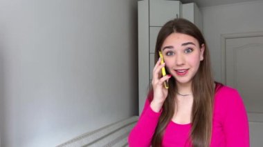 Genç bir kadın telefonda mutlu bir şekilde konuşuyor. Beyaz bluz ve şortla telefonla konuşuyor. Uzun saçlı, esmer, mutlu bir şekilde gülümsüyor. Sosyal ağlar, çevrimiçi sohbet biçimi