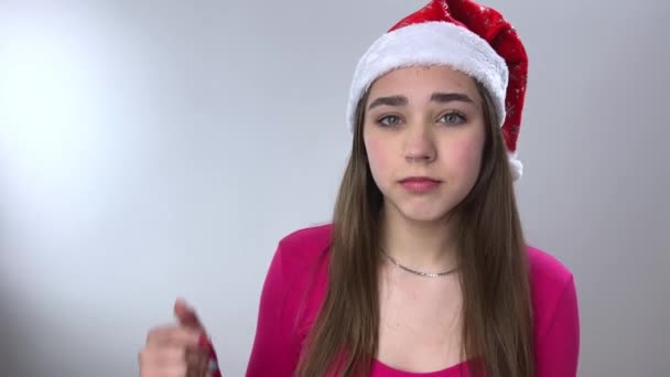 驚き見てここで興味クリスマスの帽子の若い女の子ショー彼女は彼女の指をフレームに向けるカメラに彼女の母親は右私たちを見ているようです — ストック動画
