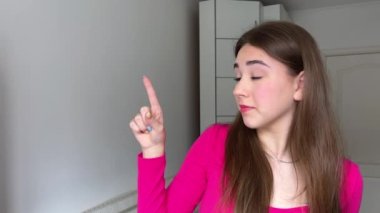Amerikalı kız işaret parmağıyla kamerayı işaret ederek el hareketleriyle davet ediyor. Etnik açıdan mutlu genç bir kadın bir şey göstermek ve vücut dili konuşmak için arıyor. Hey sen, buraya gel. Olumlu kadın gülümsüyor