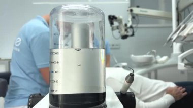 Diş hekiminin muayenehanesinde hastasıyla konuşurken ve onu tedaviye hazırlarken çekilmiş tıbbi bir görüntüsü var. Dişçi koltuğunda ciddi bir adam doktora bakıyor ve bir şey istiyor.