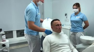 Diş hekimliği yapan bir adamın kafasının altına beyaz bir yastık yerleştirilir. Kafasının ve boynunun şeklini alır. Bisküviler diş sağlığı kliniğinde diş protezleri takar.. 