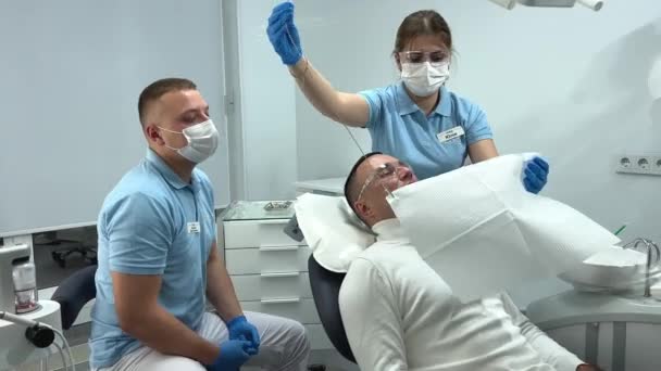 Προετοιμάζοντας Έναν Ασθενή Μια Νοσοκόμα Οδοντιατρική Κλινική Ντύνοντάς Τον Σαλιάρα — Αρχείο Βίντεο
