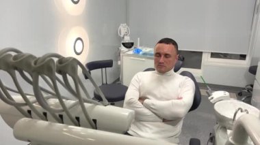 Yakışıklı bir adam diş sağlığı ocağında oturuyor. Beyaz süveter giyiyor. Her şey beyaz ve son teknoloji ürünü.