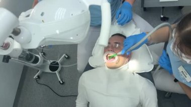 Diş sağlığı kliniği doktorları ve hemşireleri tedavi ediyor. Hepsi kameradan çekim yapmakla meşguller. Yavaşça tükürük püskürtücüden geçiyorlar.