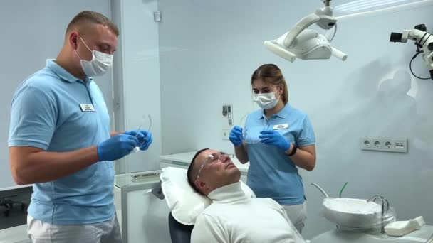 昂贵的牙科诊所专业设备医生和护士戴上眼镜 他们站在病人旁边 所有穿着浅蓝色和白色衣服的人都准备好了刷牙 — 图库视频影像