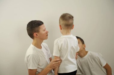 Küçük çocuk 5 yaşında ağlar parmaklarıyla gözlerini ovuşturur 2 ağabeyi 10 ve 12 yaşlarındayken bu beyaz arkaplanlı beyaz tişörtlerin ardından ona bak lütfen ağlama