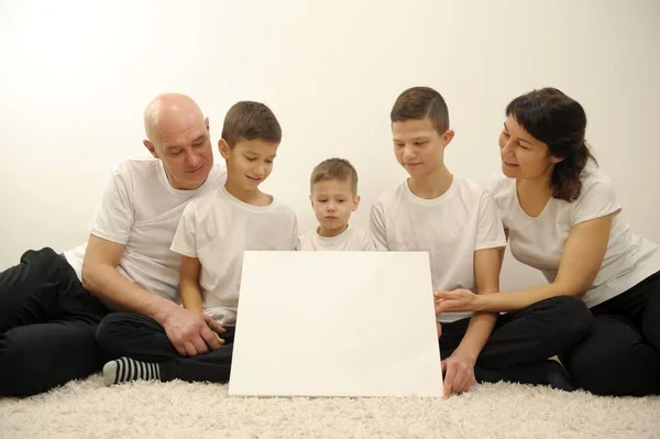 family with white board, pointing or presenting empty white placard family of five holding paper poster you can write your ad on it they look at the banner and smile at them white t-shirts