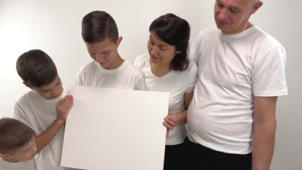 白い板のついた家族5枚の紙のポスターの空の白いプラカードの家族を指して提示するあなたはそれにあなたの広告を書くことができます彼らはバナーを見て 彼らに笑顔白いTシャツ — ストック動画