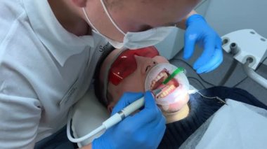 Steril eldiven diş kliniği. Bir erkek doktor başka bir adamın dişlerini fırçalıyor. Elinde özel bir yüksek teknoloji aleti var.