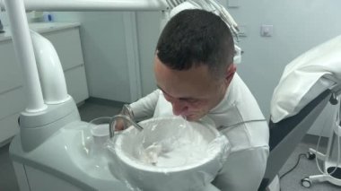 dentistry dental treatment adult man in white spits after treatment operation wipes face with a napkin dark hair light office modern latest technology prosthetics cleaning teeth wash teeth sink